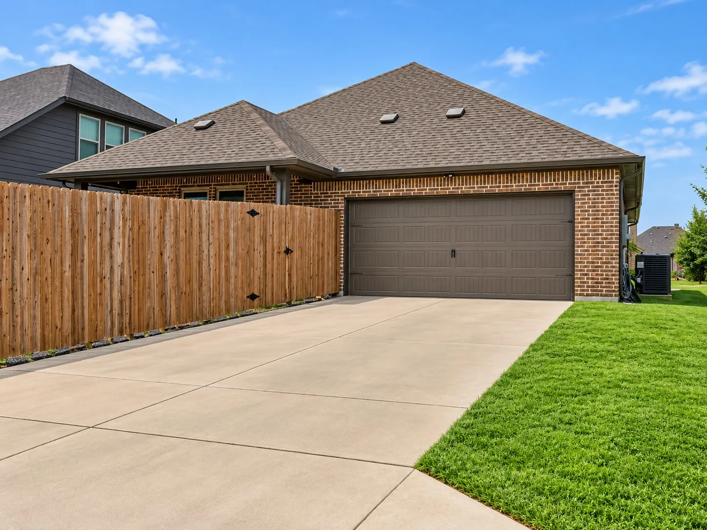 Brick exterior with a brown garage door, concrete driveway, and a wood fence