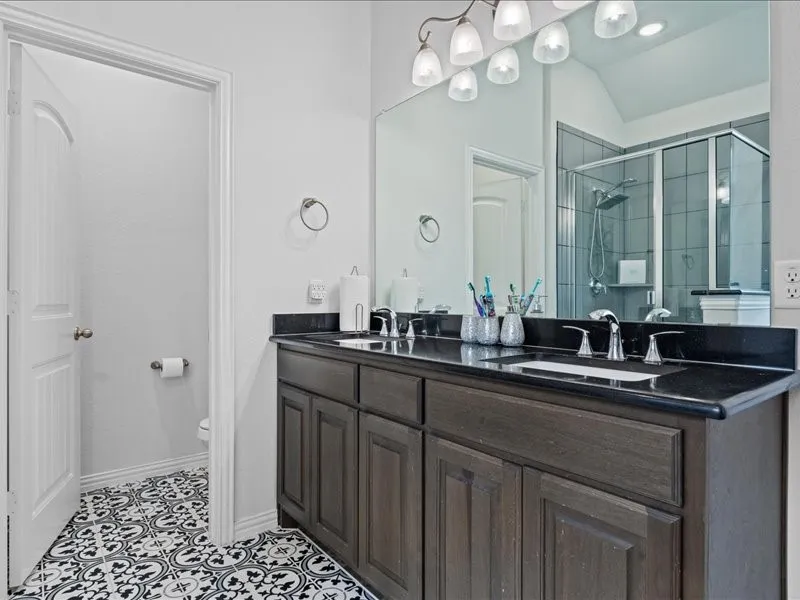 Double vanity with dark wood-finish cabinetry, black countertops, and dual undermount sinks