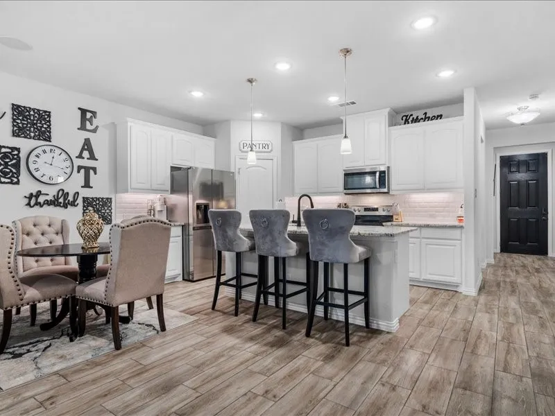 Kitchen featuring white cabinetry, stainless steel appliances, a center island with bar seating, pendant lighting, and wood-finish flooring