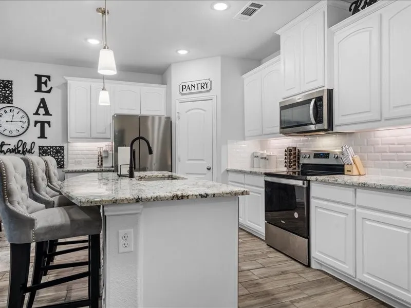 Kitchen featuring a spacious island, white cabinetry, granite countertops, stainless steel appliances, and wood-finish flooring