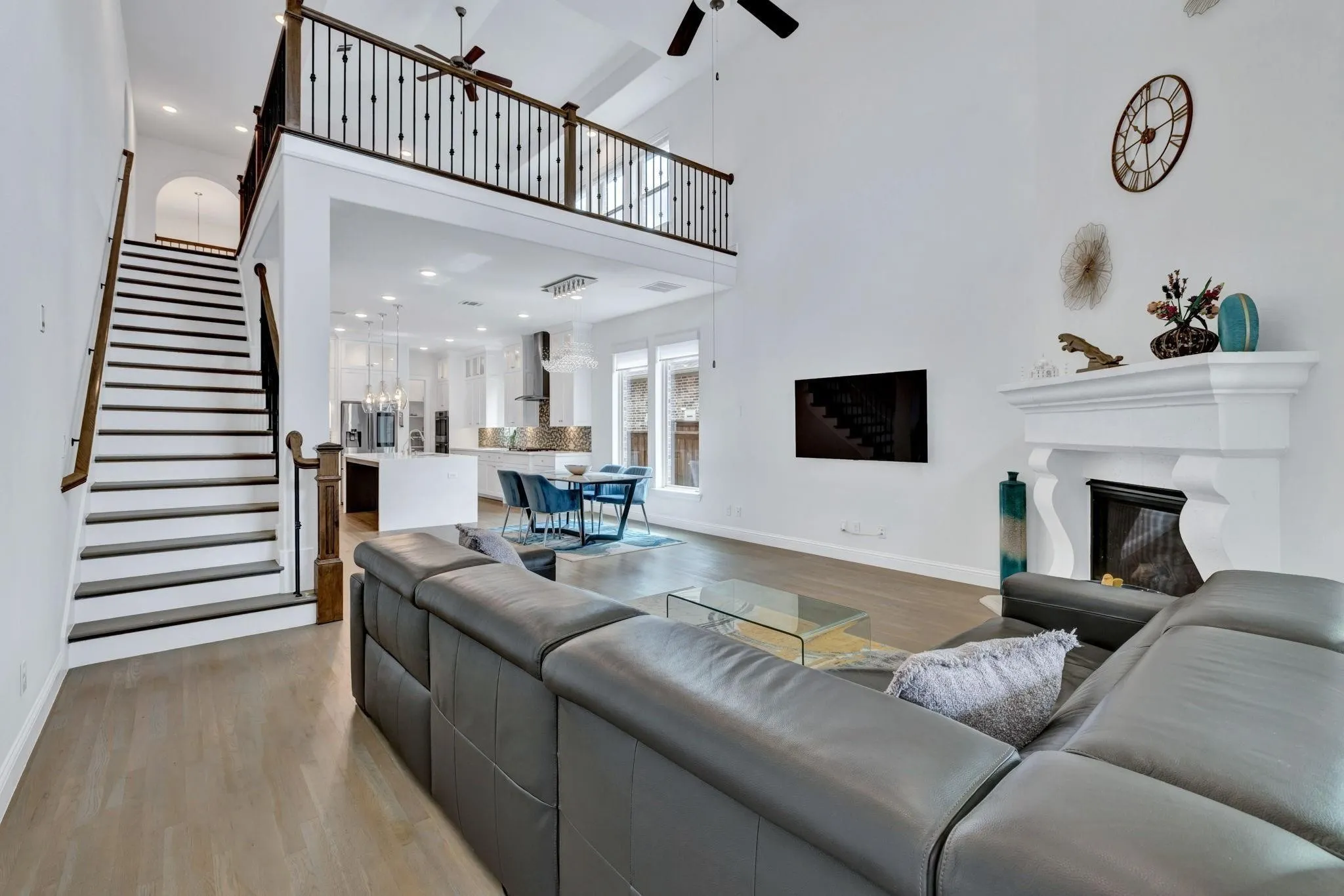 Two-story living space with a fireplace, a second-story balcony, wood-finish flooring, and a staircase with dark wood-finish treads and white risers