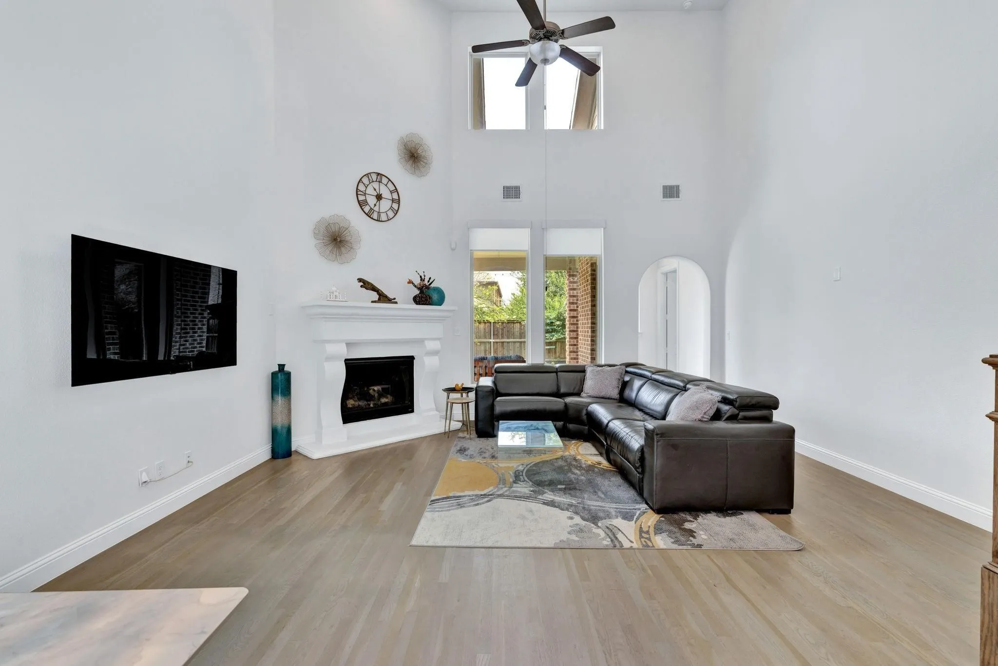 Soaring ceilings, corner fireplace with mantel, arched doorways, wood-finish flooring, and a ceiling fan