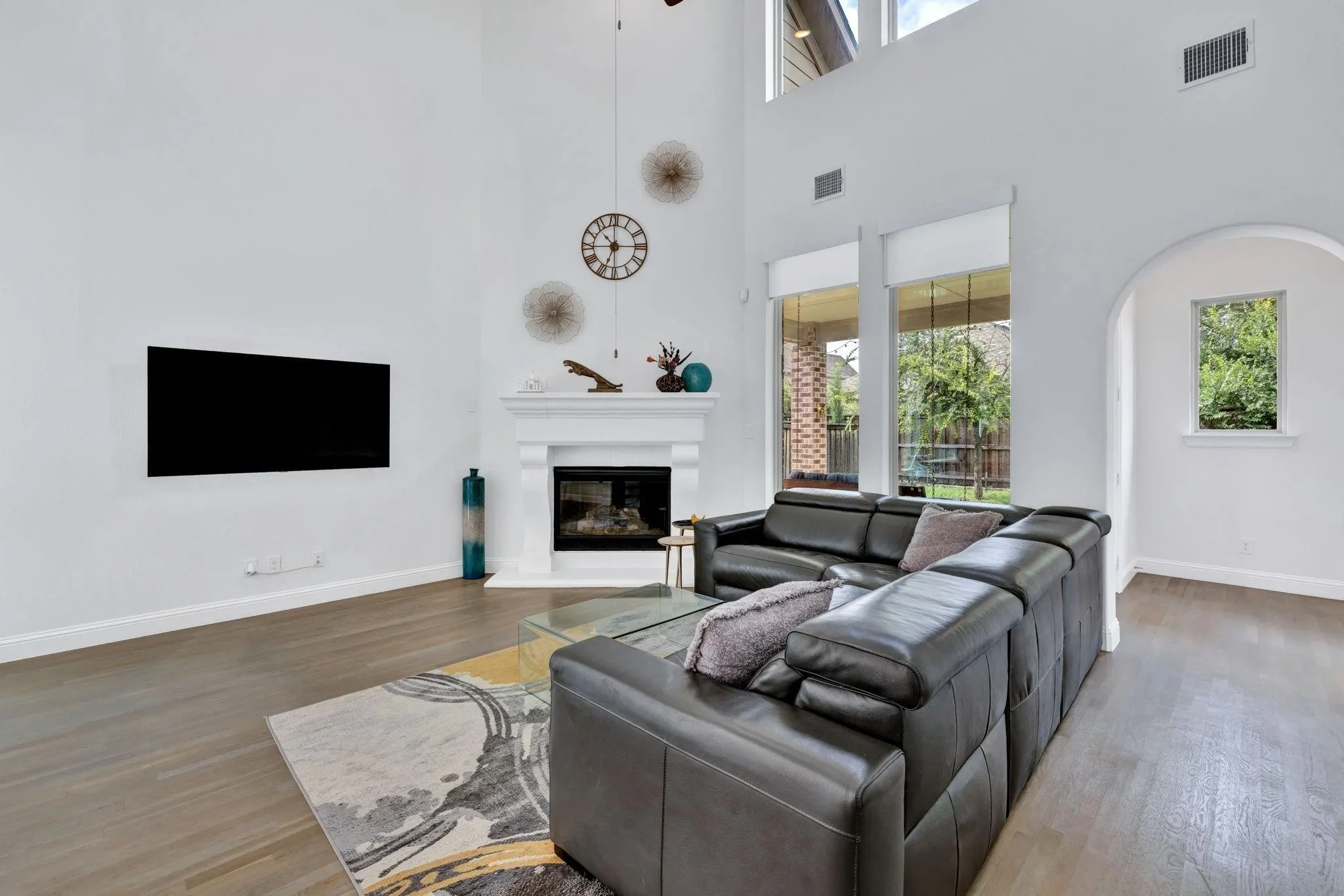 Soaring ceiling with high windows, fireplace with white mantel, wood-finish flooring, and arched doorway