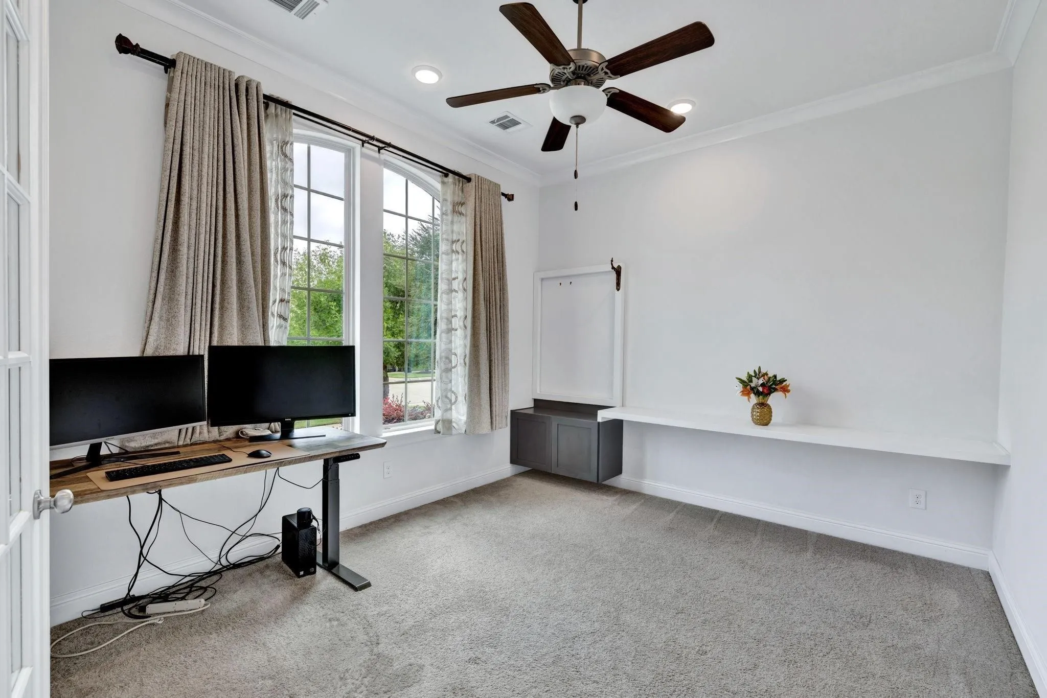Arched window with grilles, ceiling fan with light fixture, recessed lighting, crown molding, and built-in shelving with cabinetry