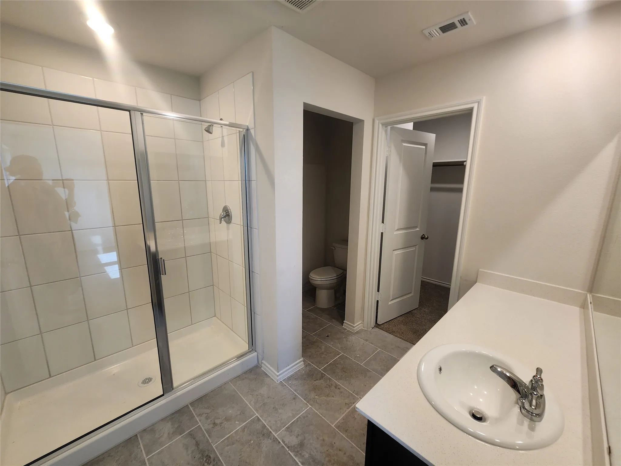 Tiled shower enclosure with sliding glass doors, single vanity with integrated sink and chrome faucet, and tiled flooring