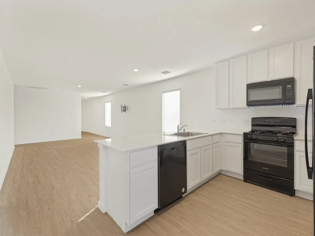 Open-concept kitchen with white cabinetry, built-in black appliances, and light wood-finish flooring