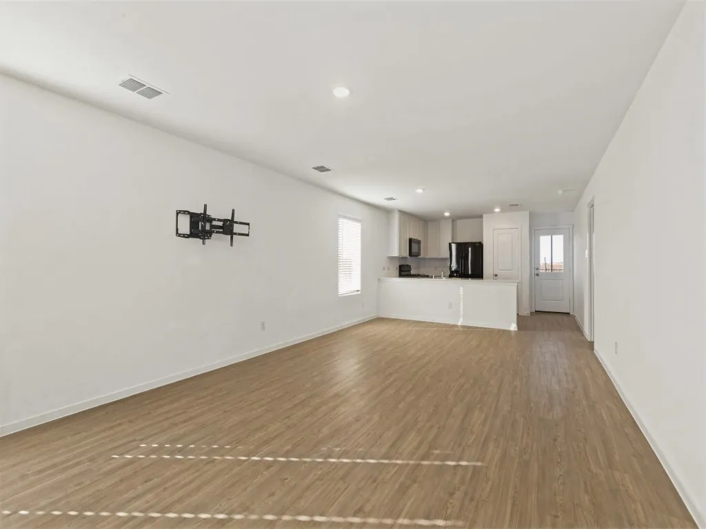 Open-concept living space featuring wood-finish flooring, recessed lighting, and a kitchen with dark appliances, light cabinetry, and a peninsula