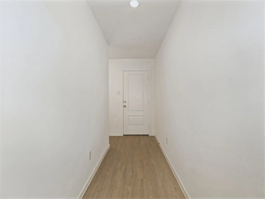 Wood-finish flooring with white baseboards, recessed ceiling lighting, and a paneled entry door with circular hardware