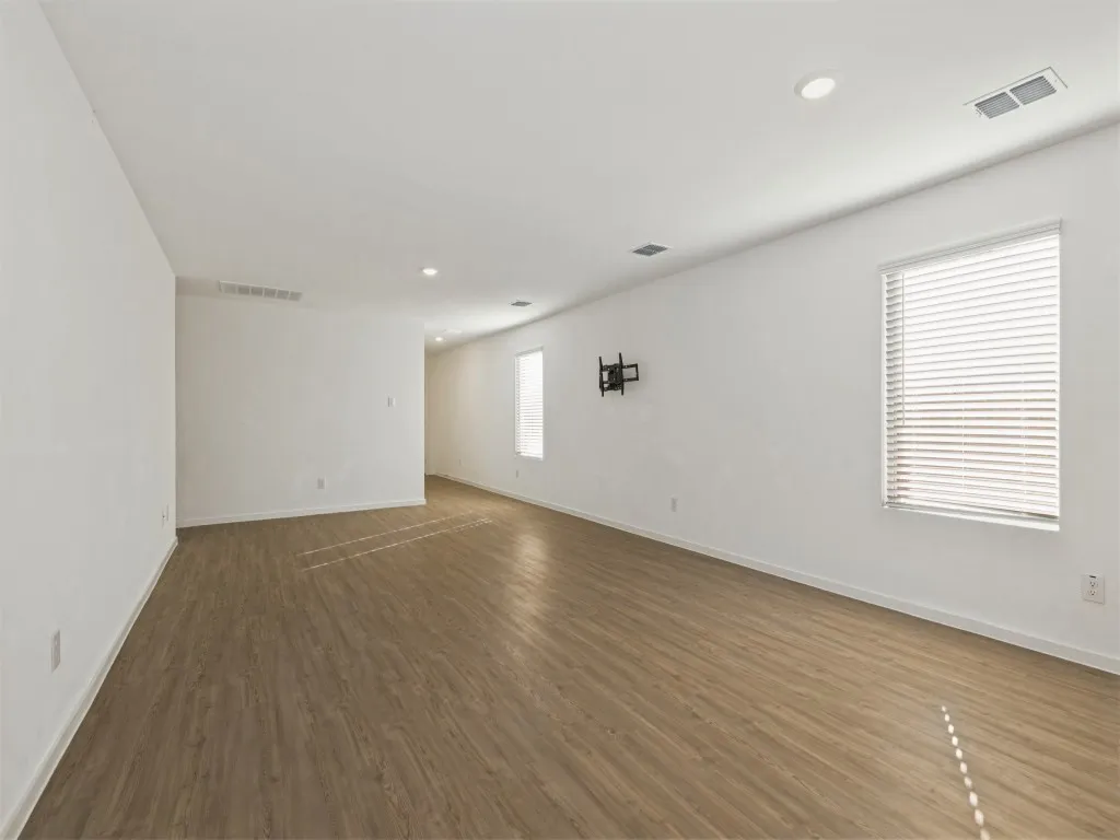Spacious room featuring wood-finish flooring, white walls, recessed ceiling lighting, and windows with horizontal blinds