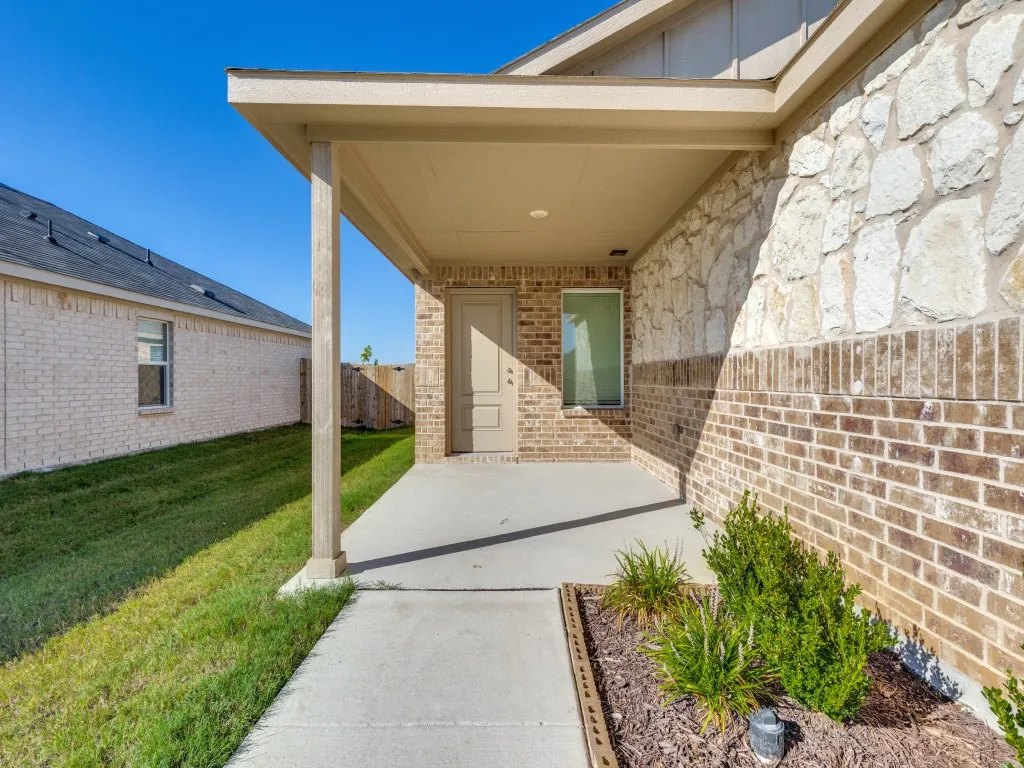 Covered patio with a concrete surface, brick and stone exterior, and a manicured lawn