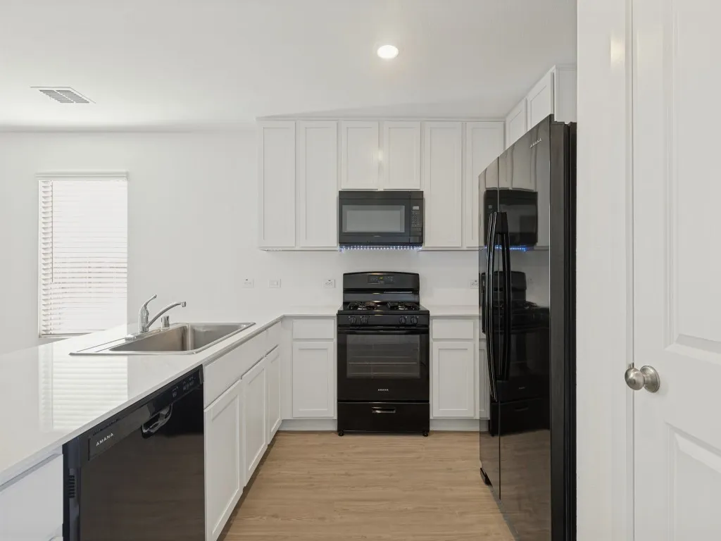 White cabinetry, black appliances, recessed lighting, wood-finish flooring, and a stainless steel sink