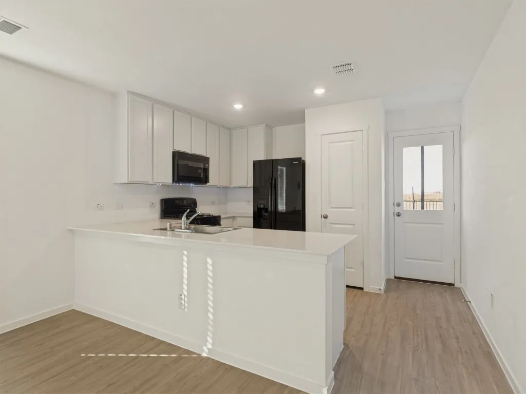 White shaker cabinetry, light-toned wood-finish flooring, white countertops, built-in black appliances, and a glass-paneled exterior door