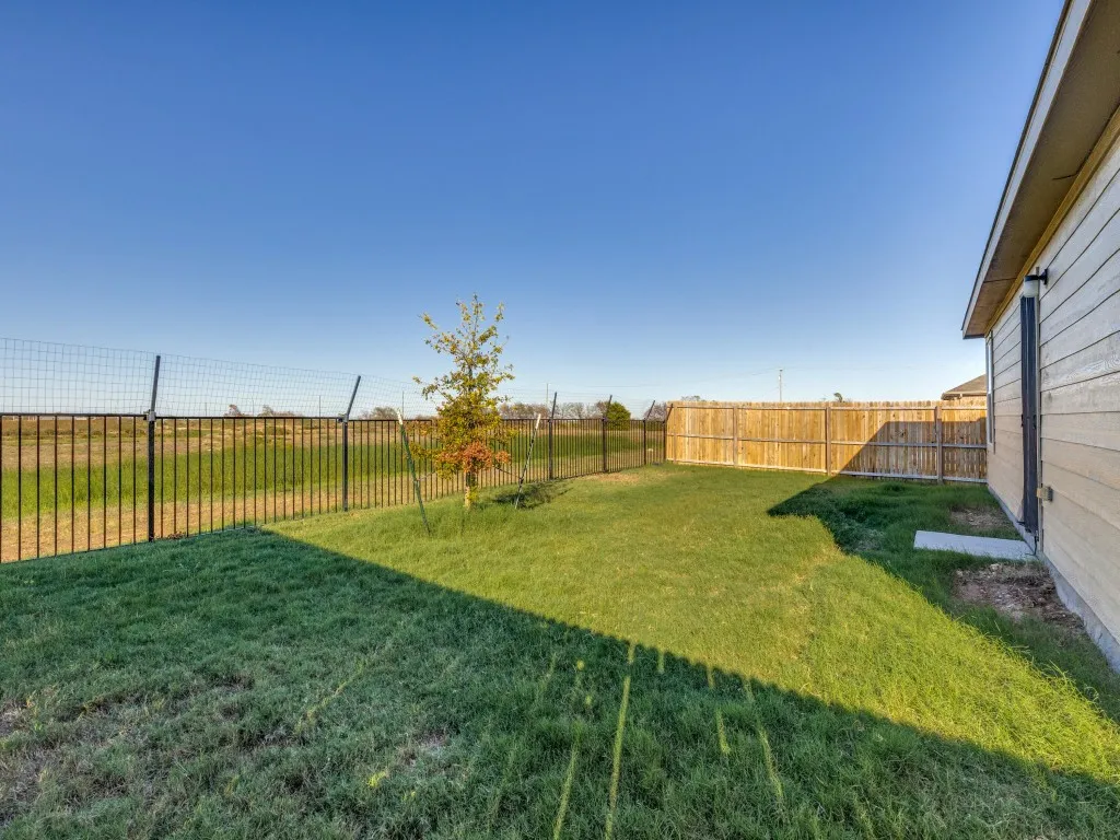 Expansive grassy area with a partial privacy fence and an open wire fence
