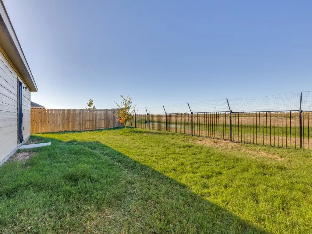 Expansive grassy yard with a wood privacy fence and a metal perimeter fence