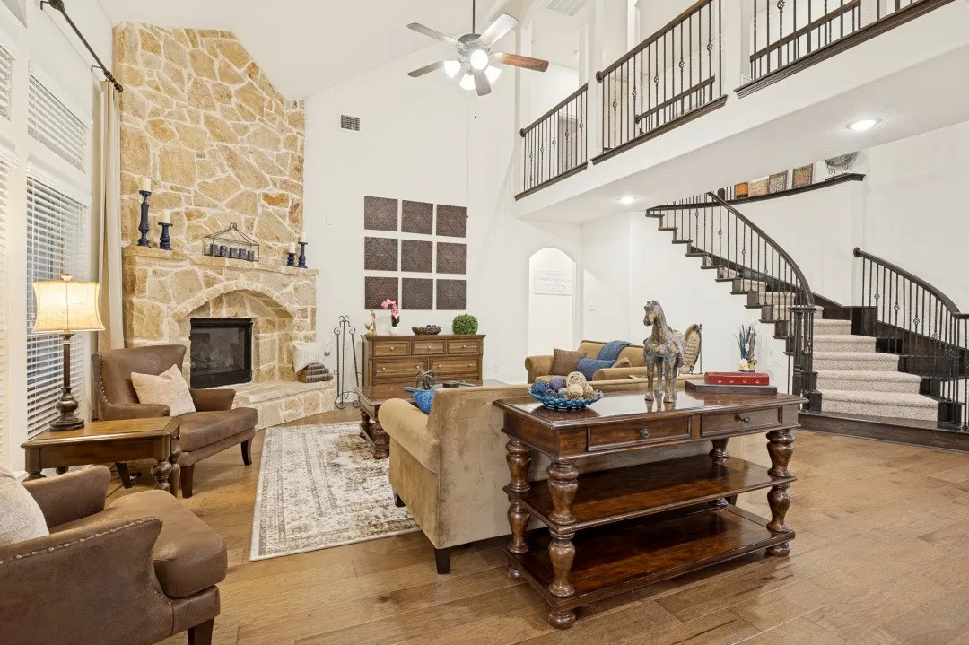 Vaulted ceiling, stone-clad fireplace, wood-finish flooring, curved staircase with wrought iron balusters, and an open upper-level walkway