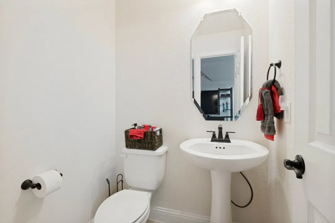 Pedestal sink with a black faucet, octagonal mirror, and white toilet