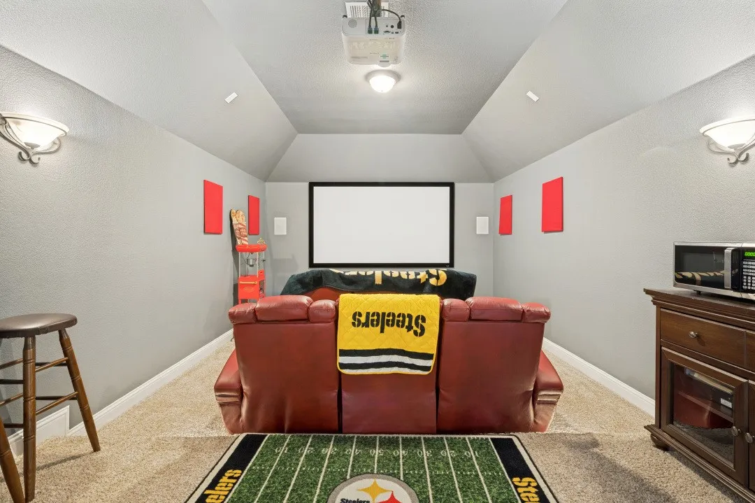 Dedicated media room featuring a mounted projector, projection screen, recessed lighting, and wall sconces