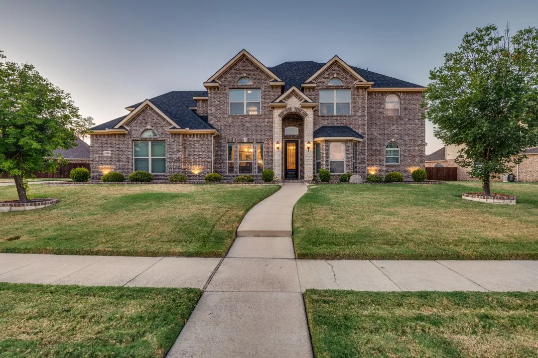 Brick exterior with stone accents, arched entryway, gabled rooflines, and a concrete walkway
