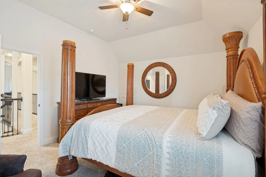 Master bedroom suite featuring a carved wood four-poster bed frame with decorative finials, ceiling fan with wood blades, and integrated flat-screen television