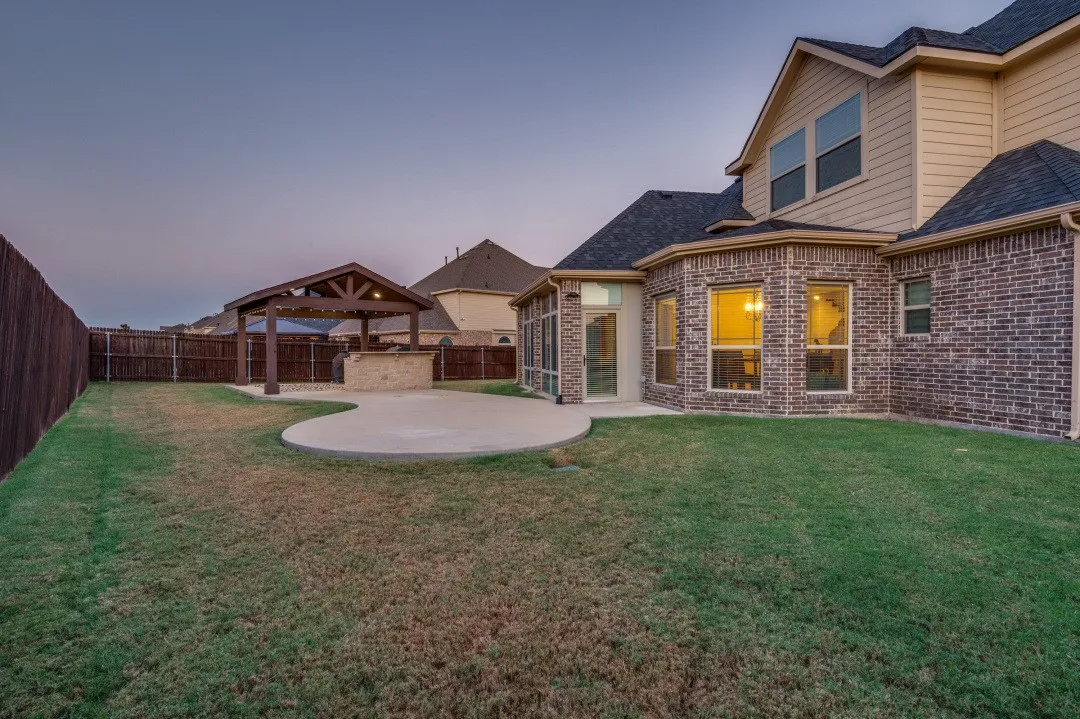 Expansive backyard featuring a manicured lawn, full privacy fencing, and a covered outdoor kitchen with a substantial patio