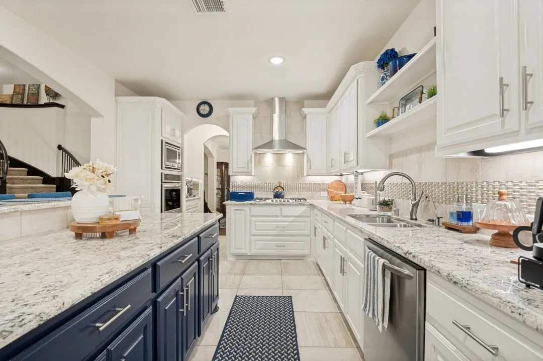 White cabinetry with stainless steel appliances, light-toned backsplash, recessed lighting, and a kitchen island with dark blue cabinetry and a light-toned countertop