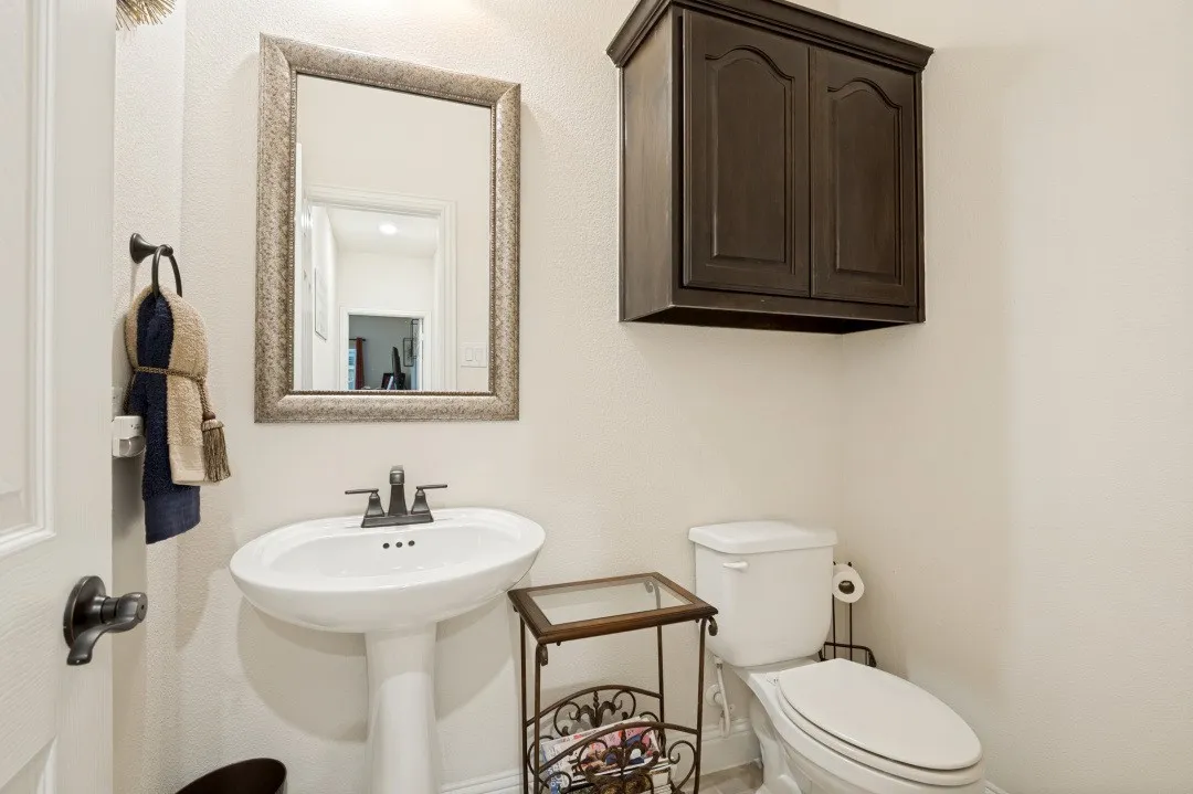 Pedestal sink with dark bronze faucet, framed mirror, wall-mounted dark wood-finish cabinetry, and white toilet