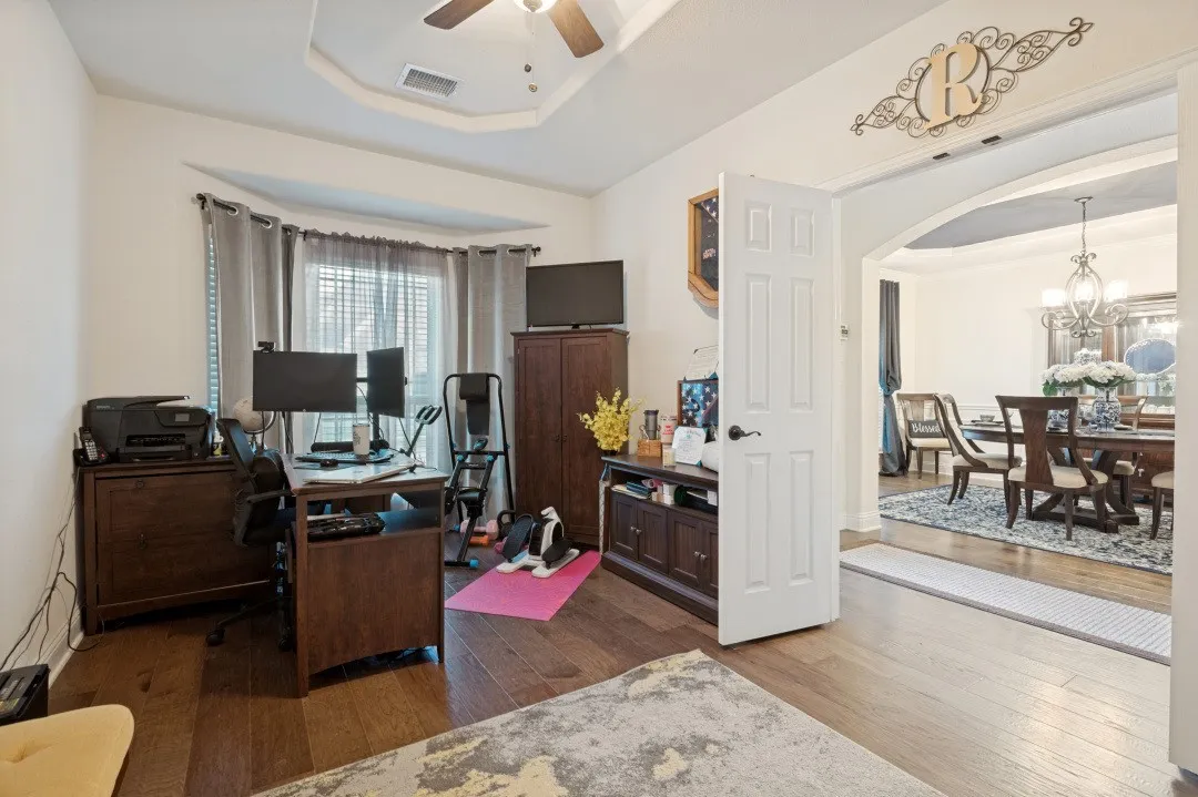 Hardwood-finish flooring throughout, tray ceiling with a ceiling fan, and an arched doorway leading to an additional space