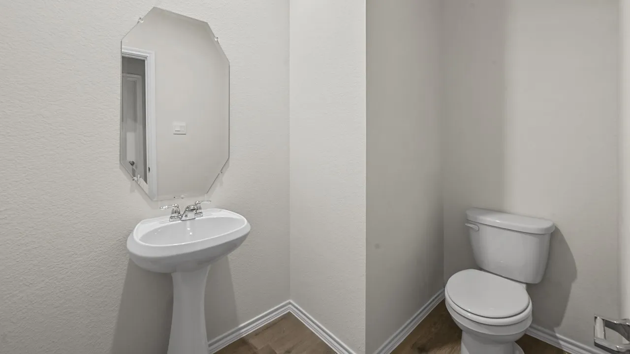 Pedestal sink with chrome faucet, octagonal mirror, toilet, and wood-finish flooring