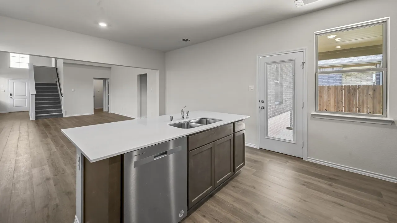 Kitchen island featuring an undermount double sink, stainless steel dishwasher, and a light-toned countertop