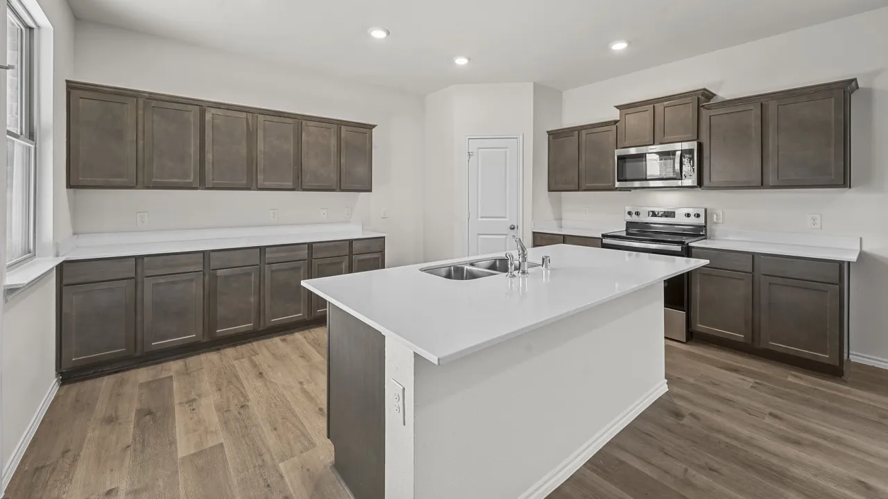 Kitchen featuring an island with dual sinks, extensive dark wood-finish cabinetry, light-toned countertops, stainless steel appliances, and recessed lighting
