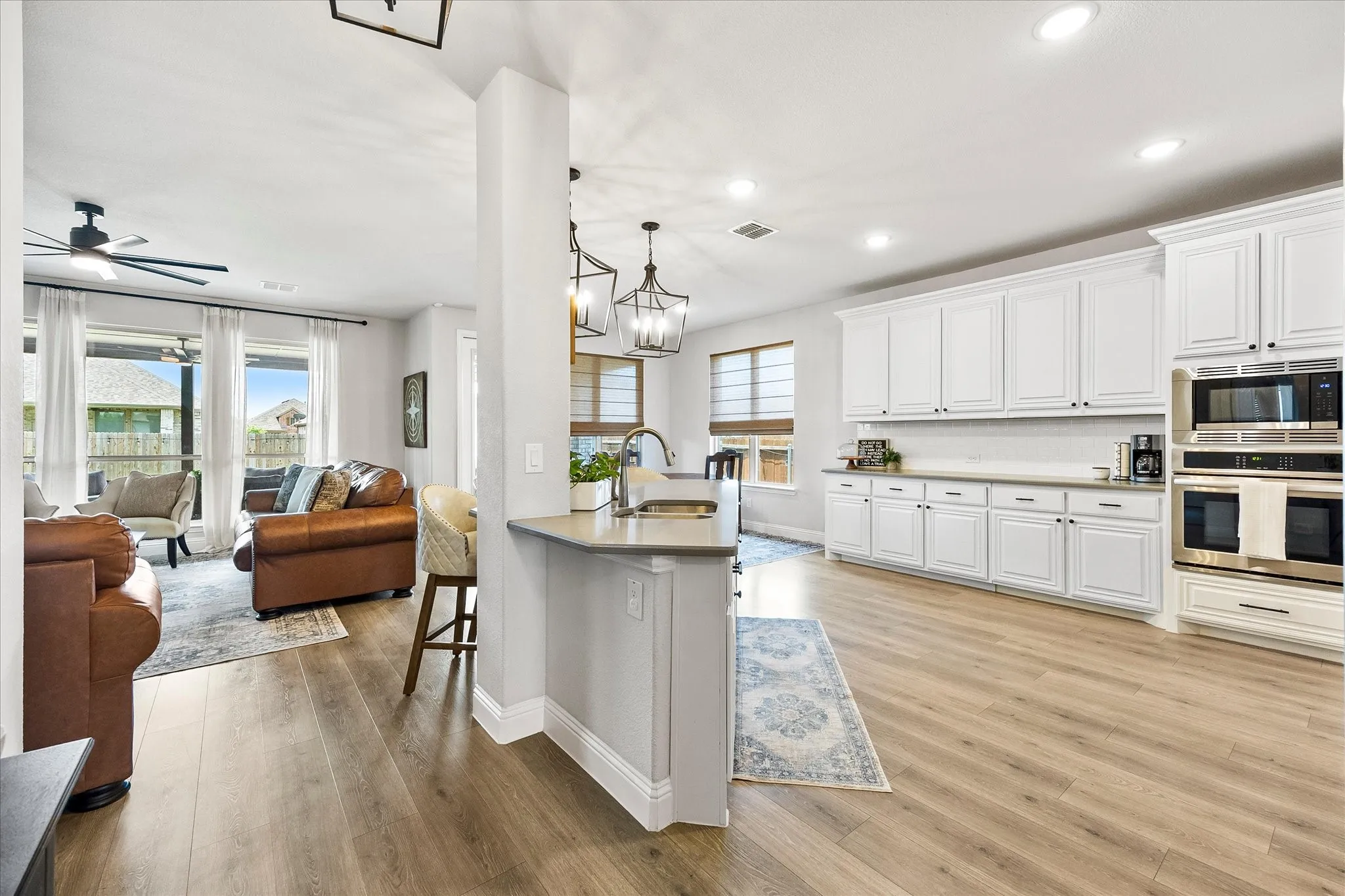 Open-concept kitchen and living area featuring wood-finish flooring, white cabinetry, stainless steel double ovens, and a built-in microwave