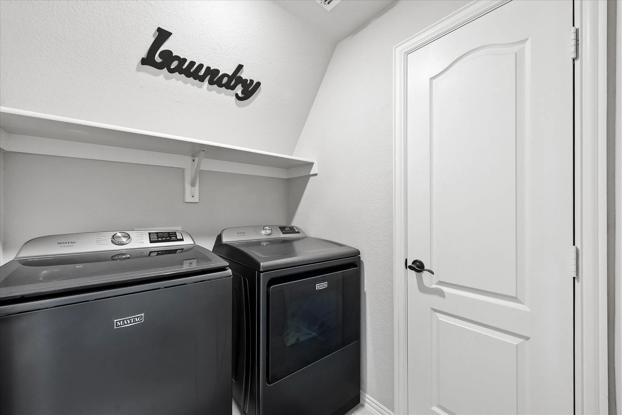Dedicated laundry area featuring a white storage shelf, door leads to attic space.
