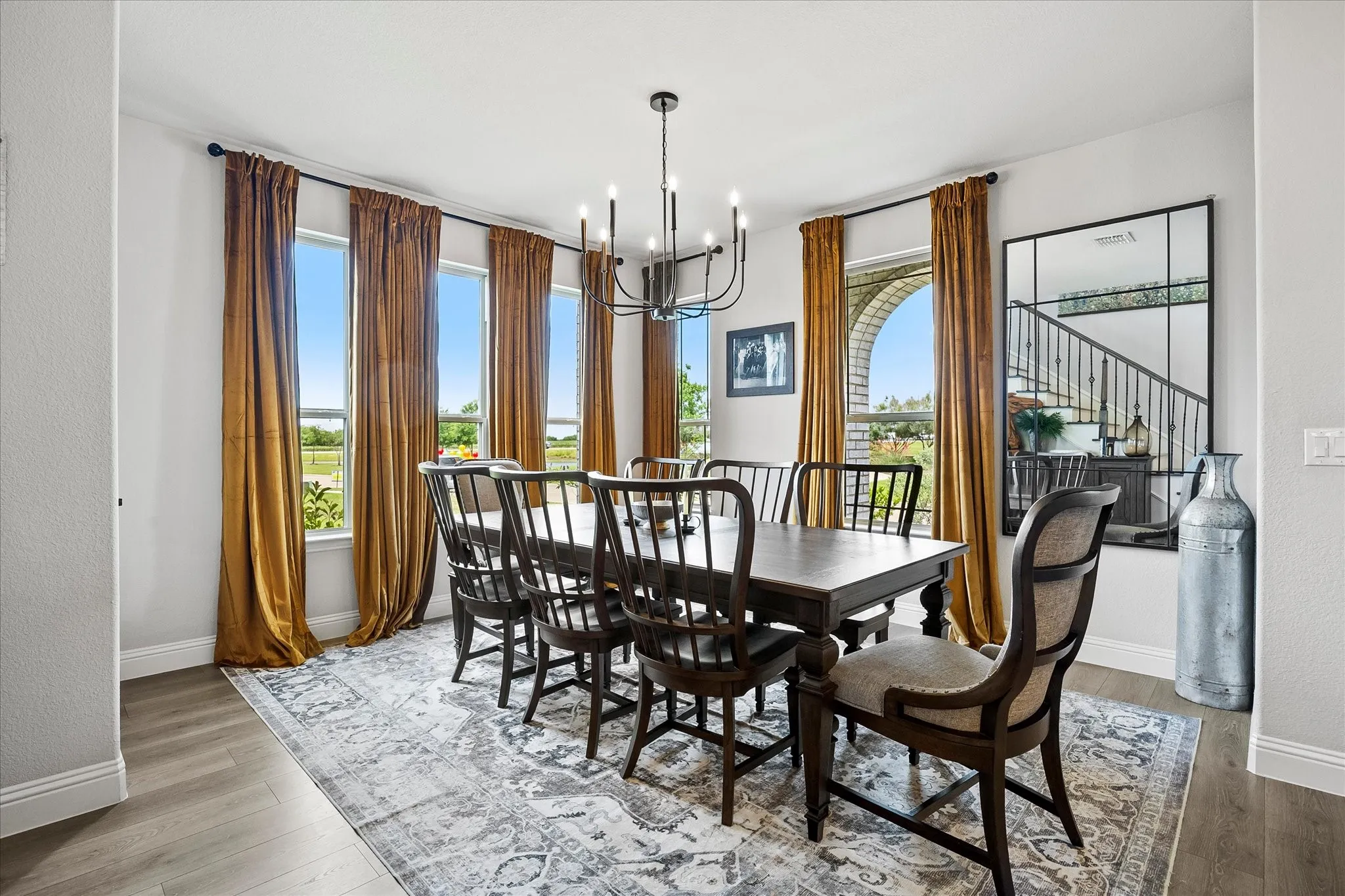 Spacious dining area featuring wood-finish flooring, a contemporary chandelier, multiple large windows, and an arched architectural opening