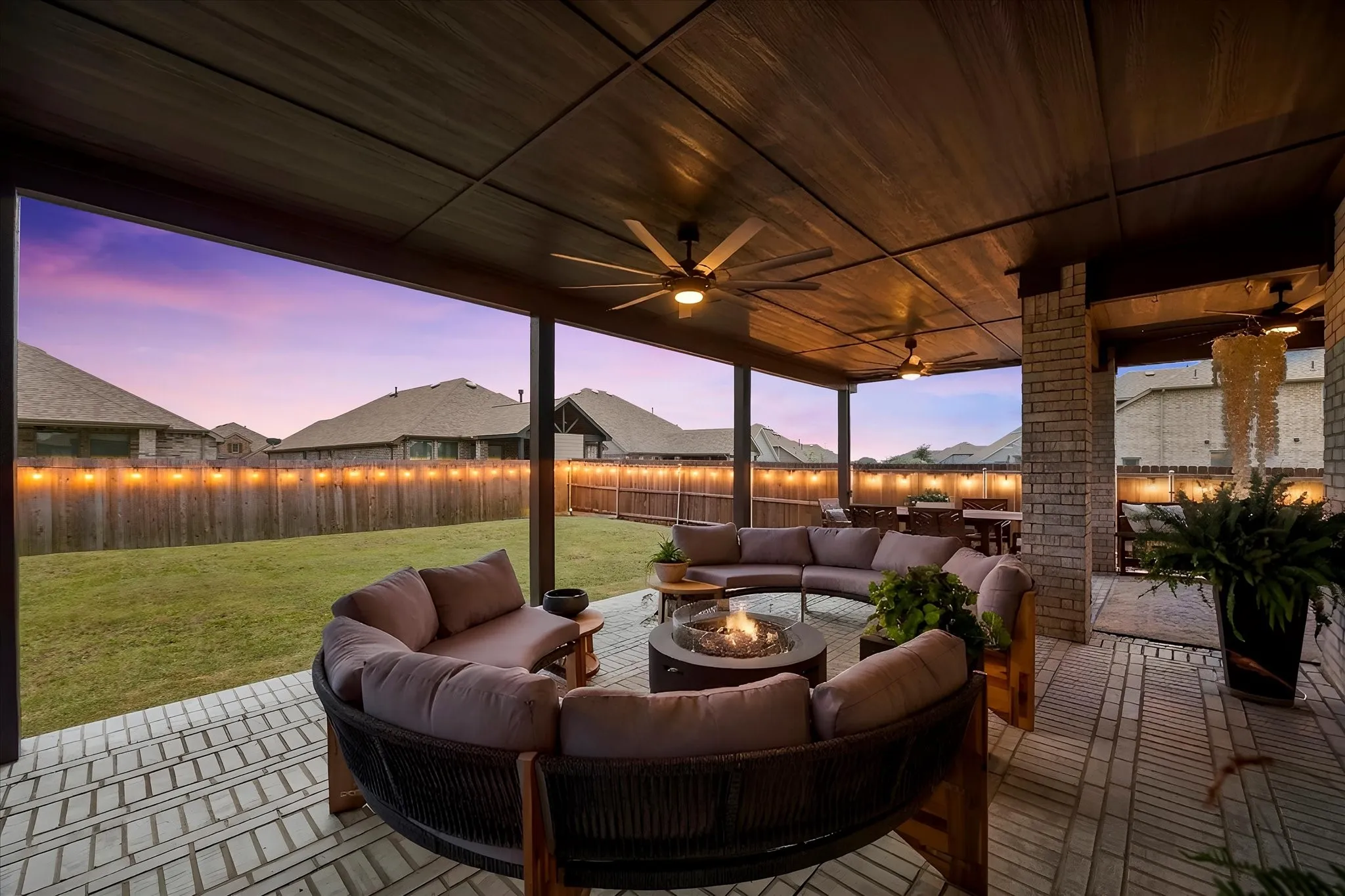 Covered outdoor patio featuring a brick-patterned hardscape, multiple ceiling fans with integrated lighting, and a wood-finish ceiling