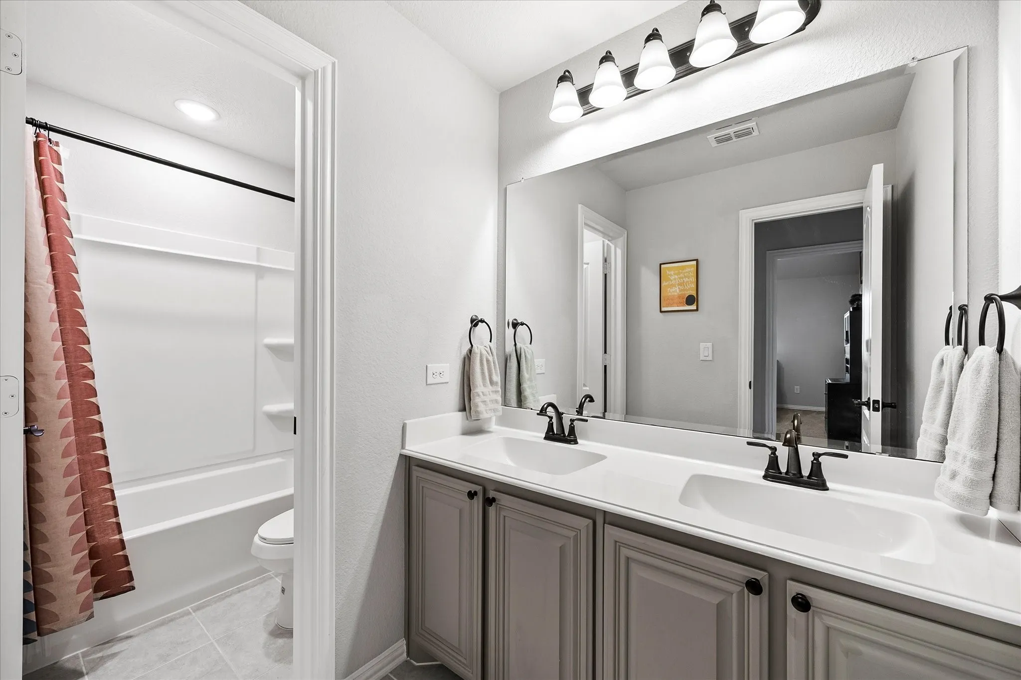 Bathroom featuring a dual-sink vanity with gray cabinetry, a full-width mirror, and a combination tub and shower