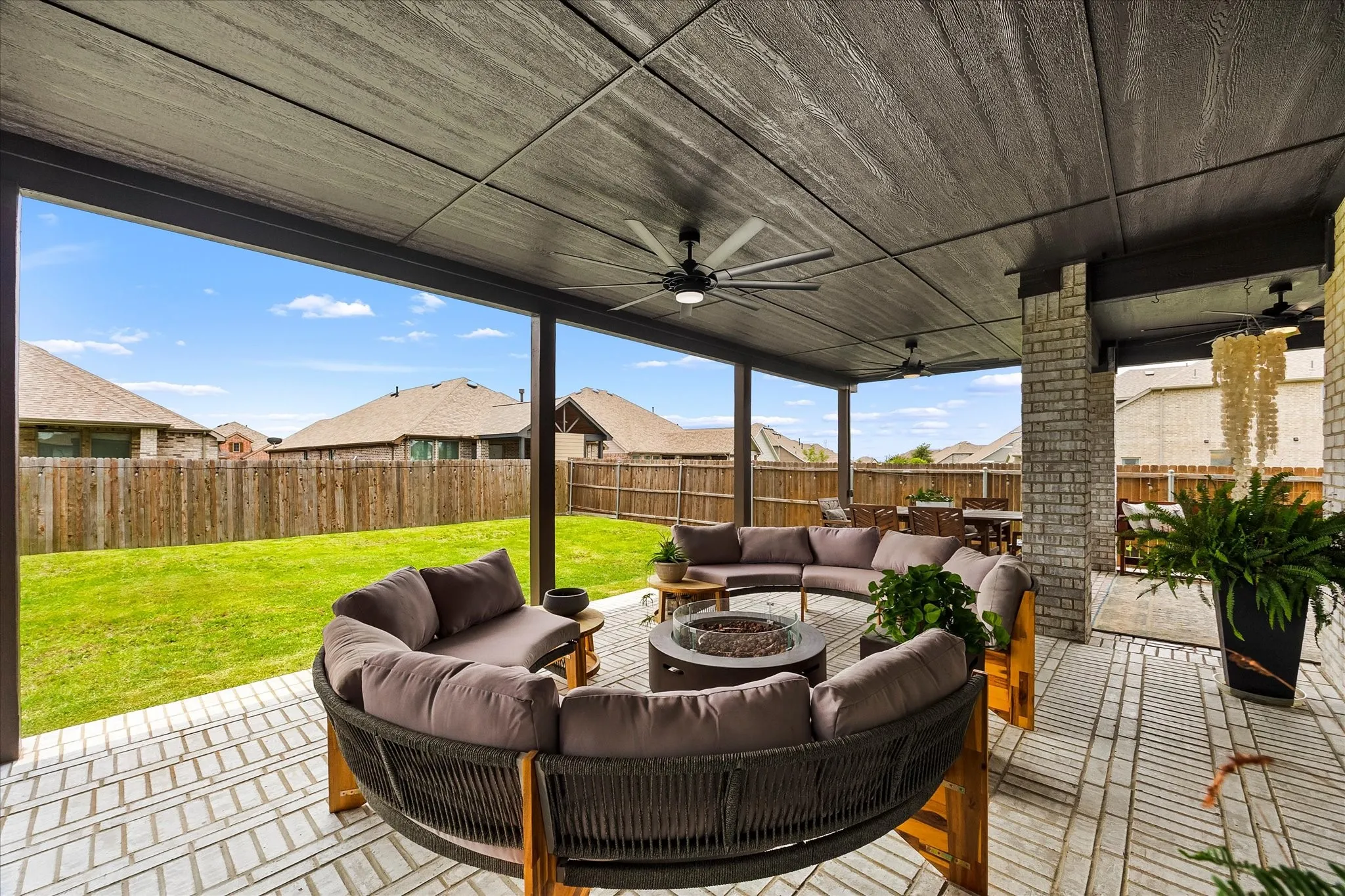 Covered outdoor patio featuring a wood-look ceiling with integrated ceiling fans, brick columns, and herringbone-patterned paver flooring