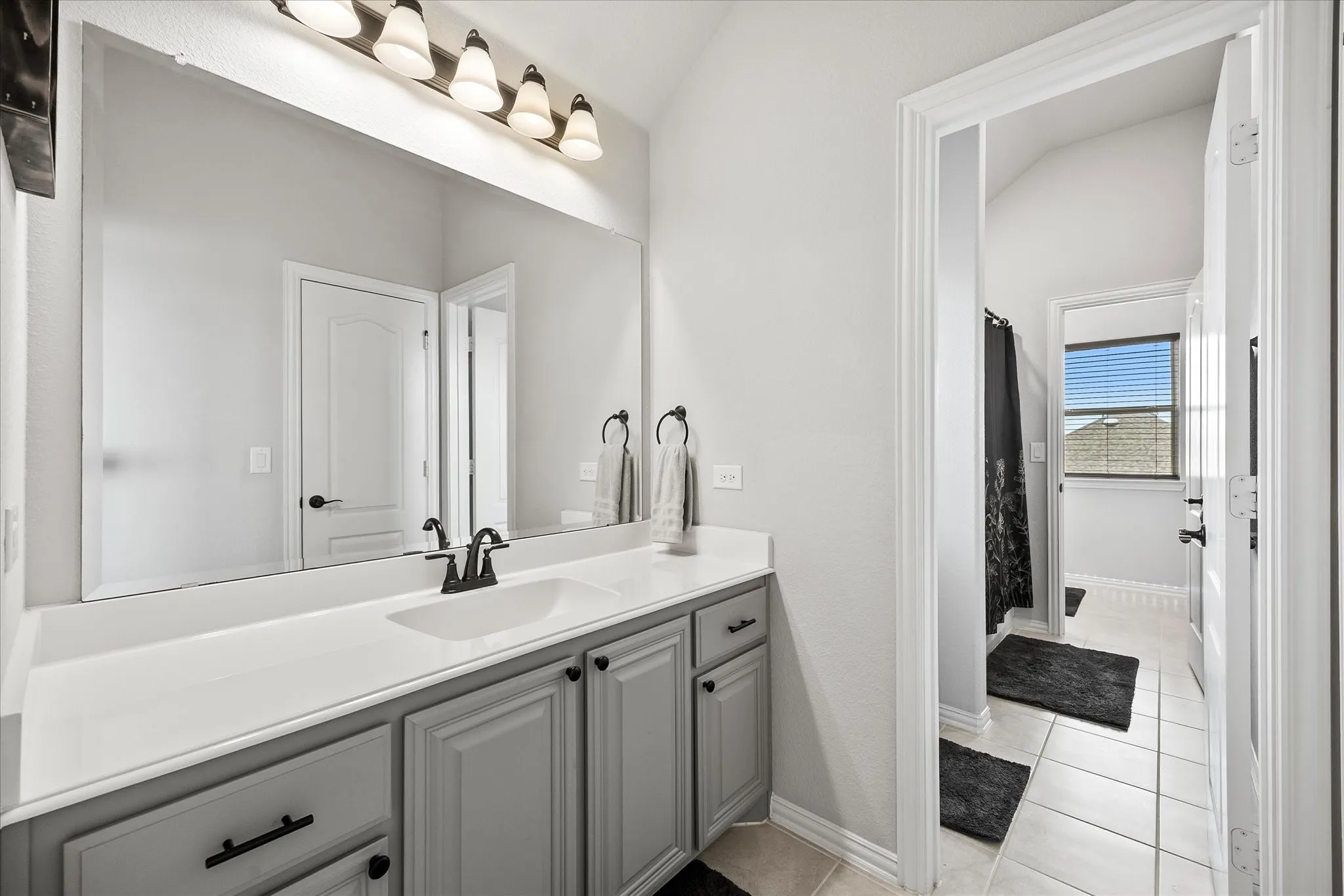 Bathroom vanity featuring a single sink, white countertop, and gray cabinetry with black hardware