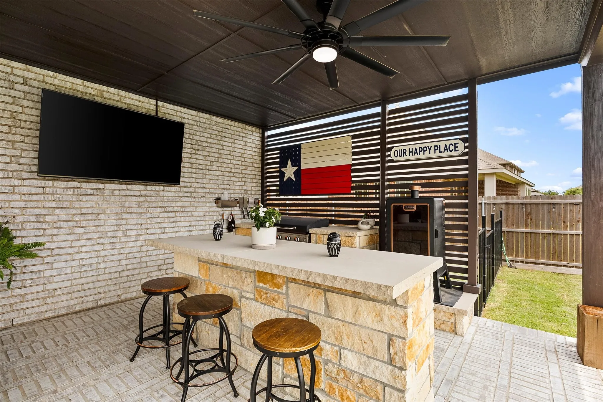 Covered outdoor living space featuring a built-in stone and countertop bar, brick-finish wall, and paver flooring
