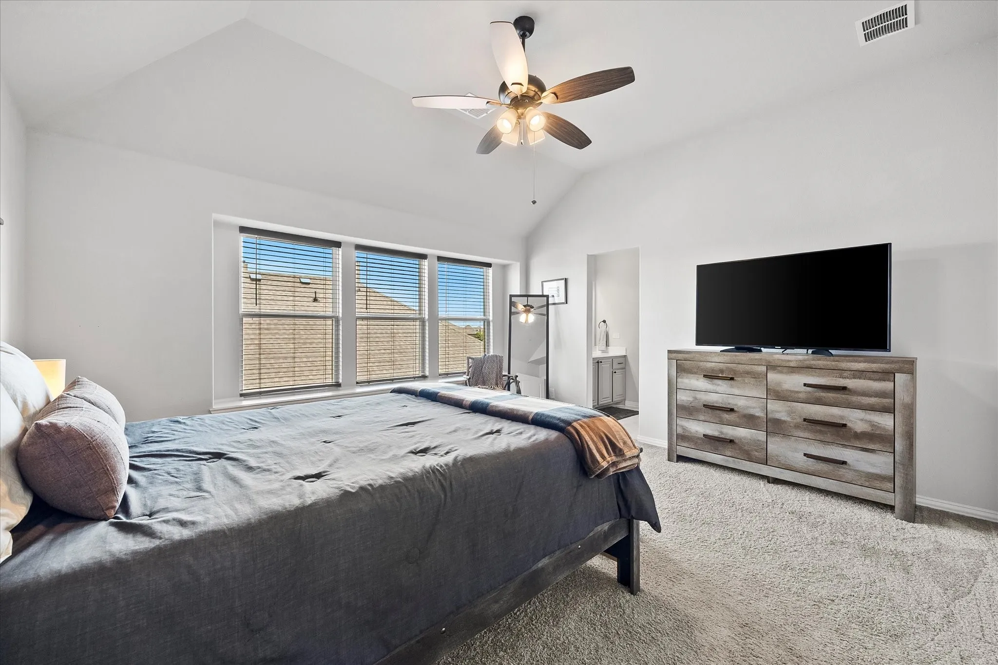 Vaulted ceiling bedroom featuring triple windows with blinds, a ceiling fan with integrated lighting, and plush carpet flooring