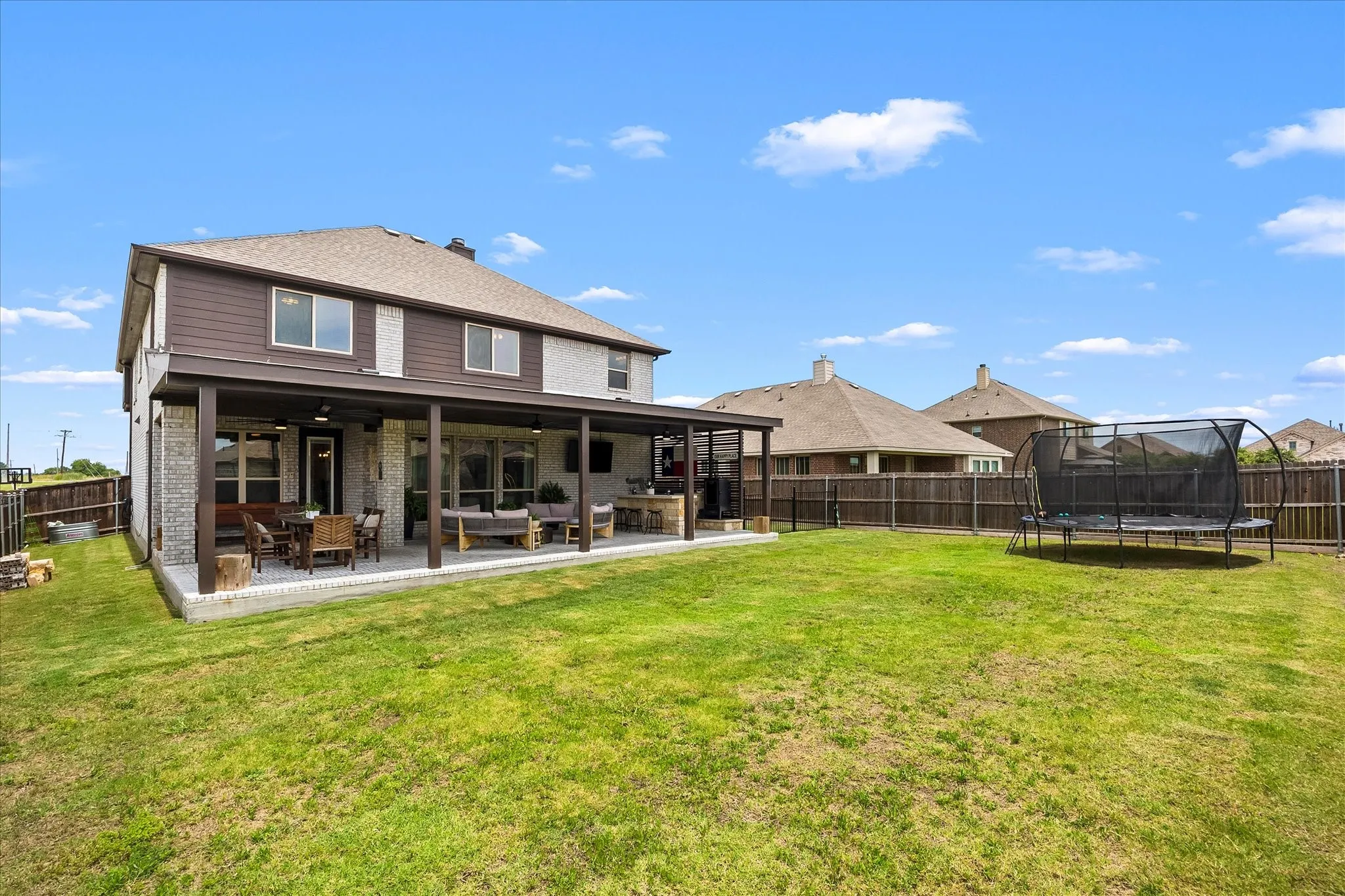 Expansive green lawn with a covered patio featuring a wood-finish ceiling, column supports, and built-in amenities