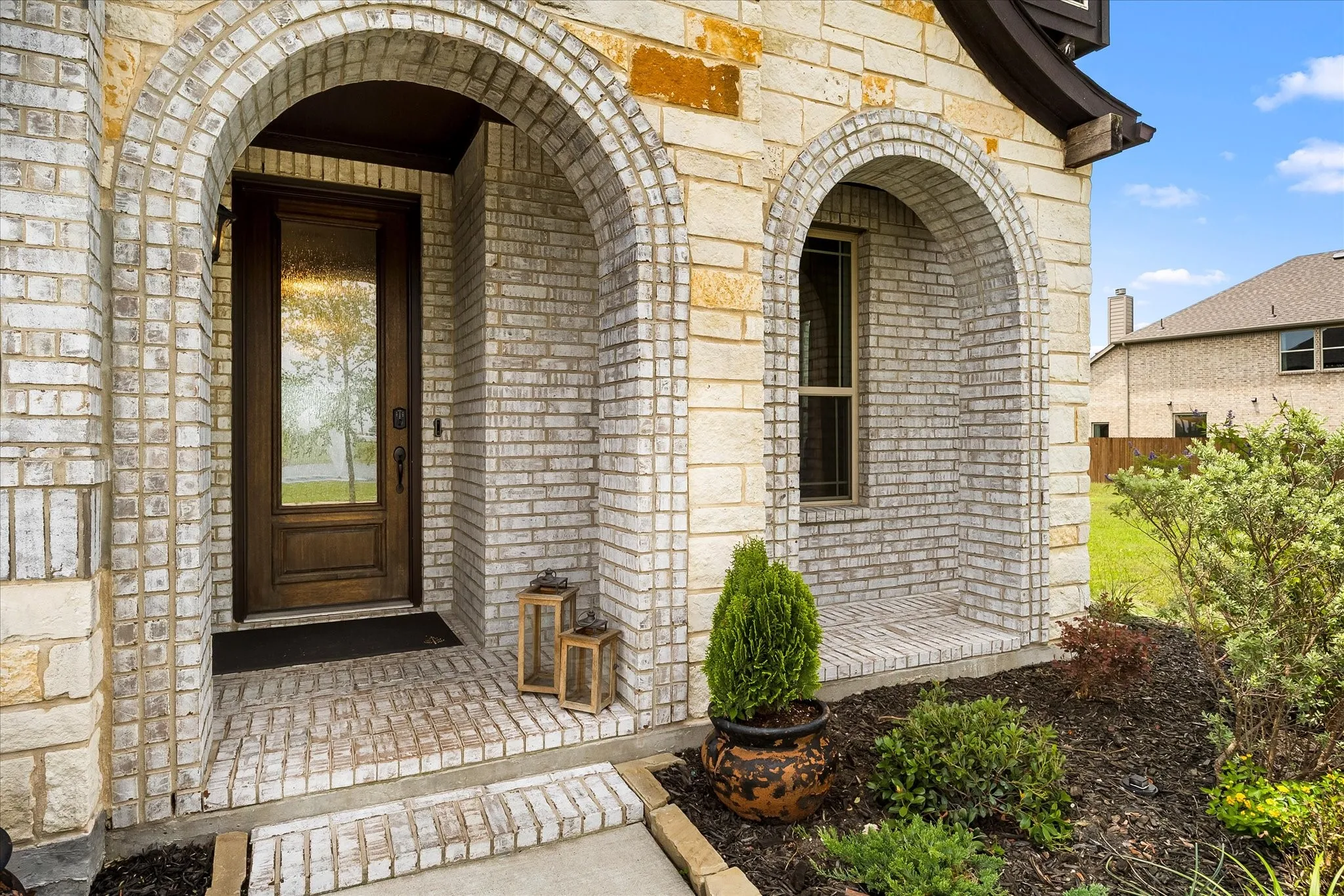 Brick and stone exterior featuring an arched entryway with a wood-finish door and glass insert