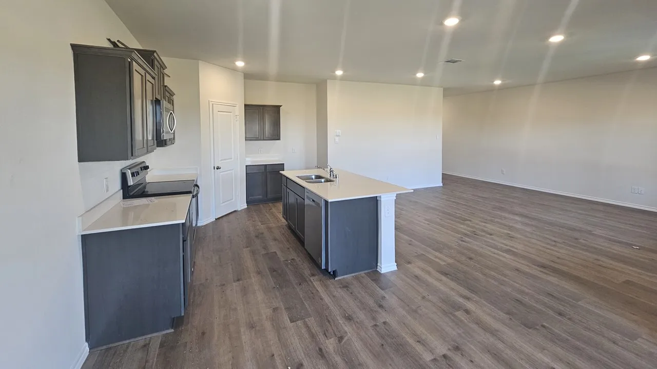Open-concept living space with wood-finish flooring, recessed lighting, and a kitchen island featuring a double-basin sink
