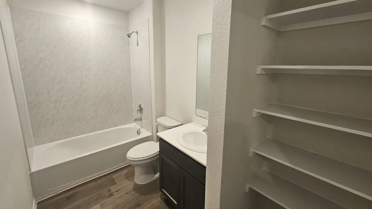 Bathroom featuring a tub/shower combination with a textured surround, a single vanity with a white countertop and dark cabinetry, and wood-finish flooring