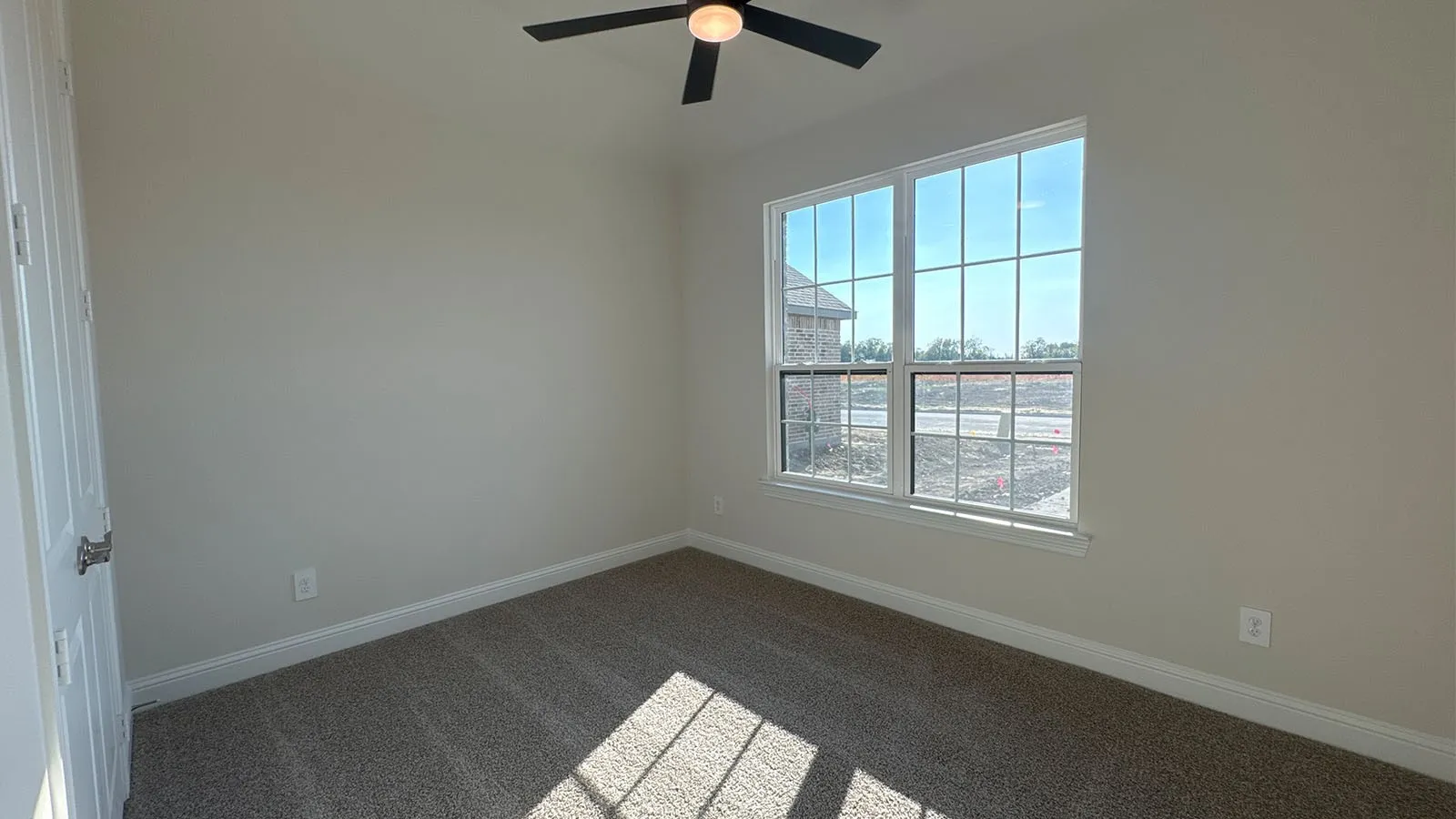 Textured carpet flooring, neutral painted walls, white door with brushed nickel hardware, and a ceiling fan with integrated lighting