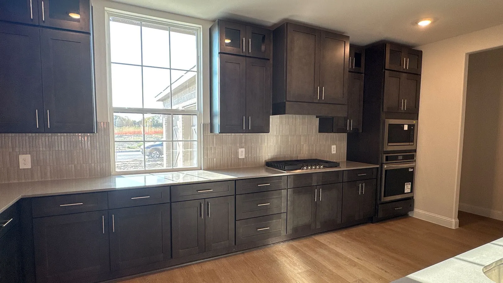Dark wood-finish cabinetry with modern hardware, integrated stainless steel appliances, light-toned countertops, and a full-height tile backsplash