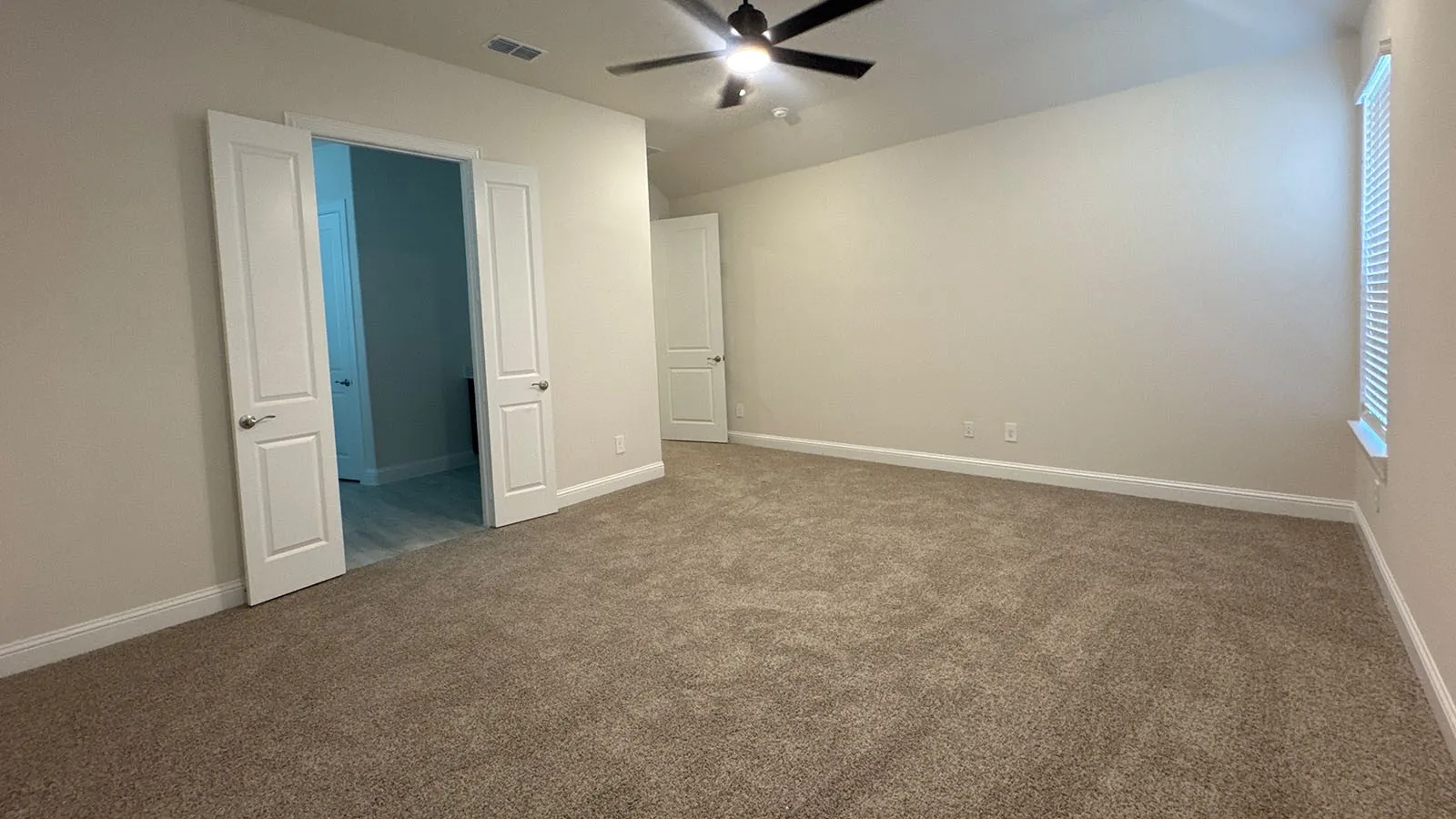 Spacious room with plush carpeting, neutral wall finishes, a ceiling fan, and double panel doors