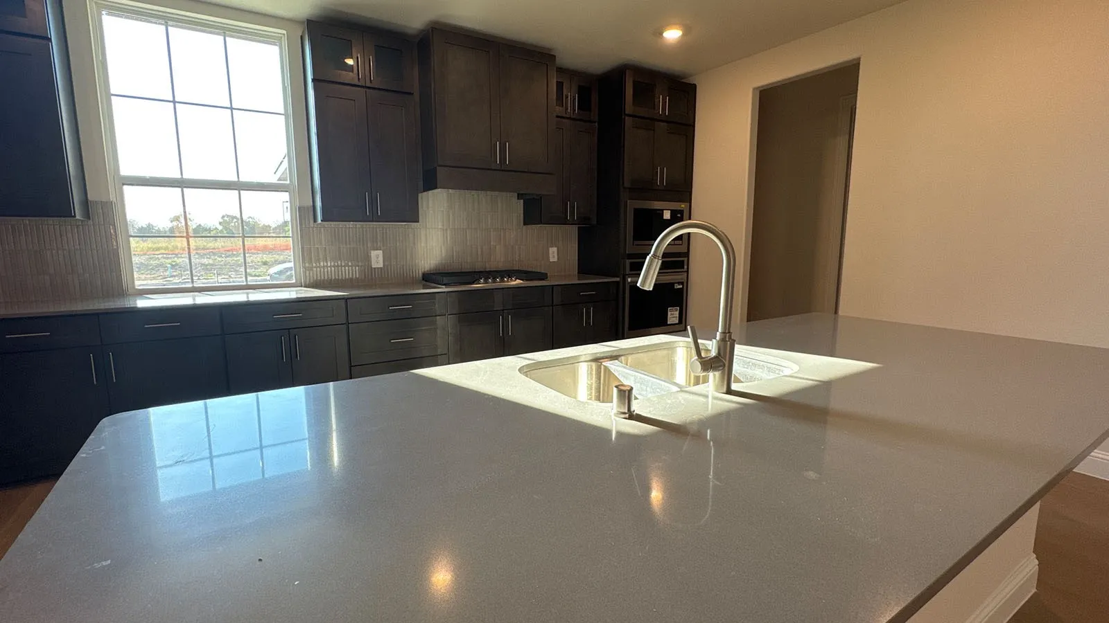 Kitchen featuring dark wood-finish cabinetry, light-toned countertops, a stainless steel sink with a gooseneck faucet, and integrated wall oven