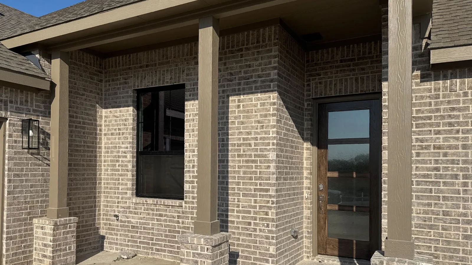 Brick exterior with a covered entry, dark-framed window, and a wood-finish entry door with clear glass panels