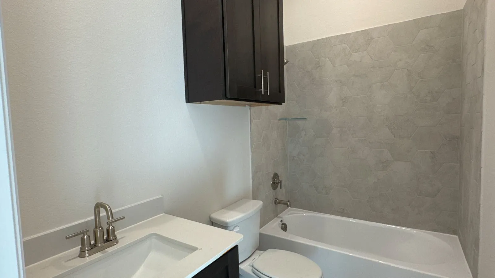 Vanity with integrated sink, brushed nickel faucet, dark wood-finish cabinetry, and hexagon tile bath surround