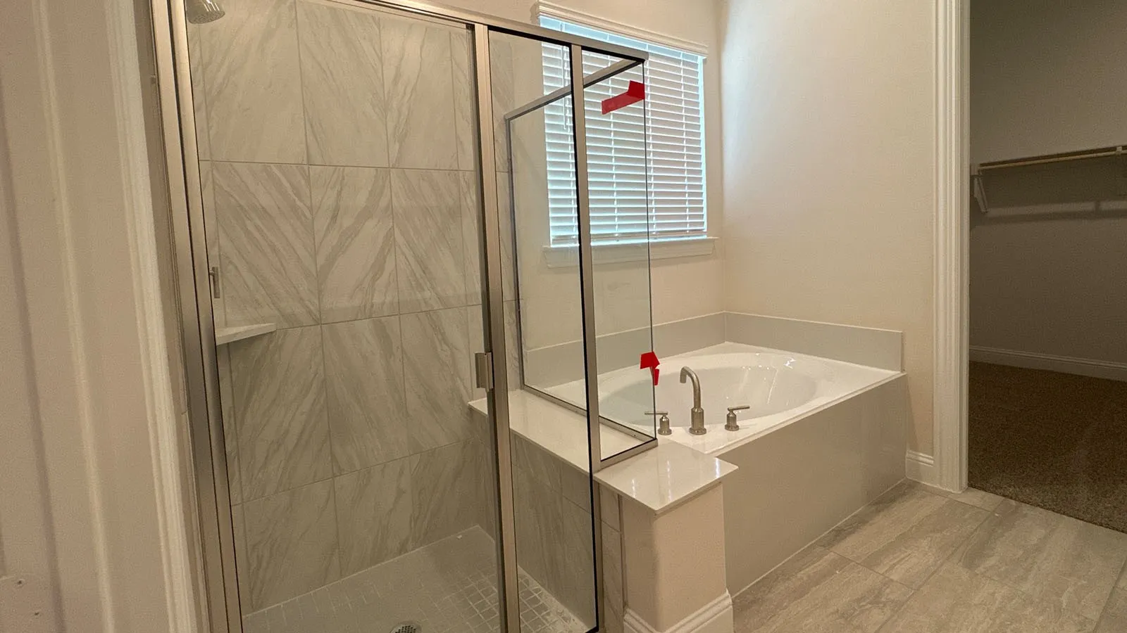 Walk-in shower with clear glass enclosure and tile surround, accompanied by a built-in soaking tub with deck-mounted fixtures, set on wood-finish flooring